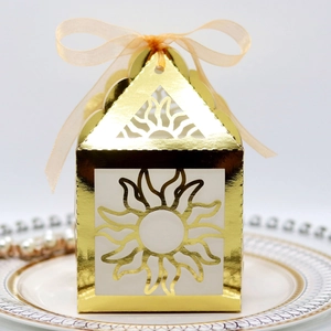 Close-up of golden hollow sun patterned gift box with orange ribbon on ceramic tray