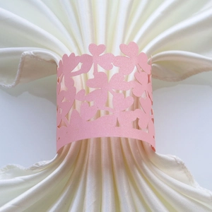 Detail of pink pearlescent paper napkin ring with laser-cut heart and clover pattern