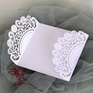Close-up of laser-cut lace pattern on white wedding invitation cover with floral details