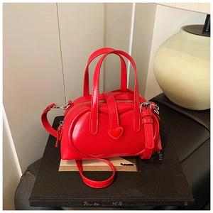 Detail view of a glossy red Boston bag with a heart patch and detachable shoulder strap