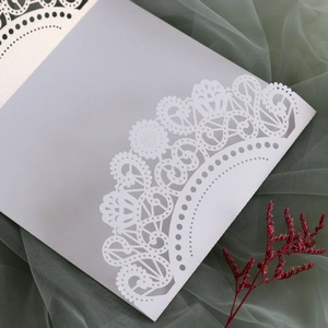 Detail of laser-cut lace floral pattern on elegant white wedding invitation sleeve
