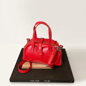 Detail of red glossy leather pillow bag featuring a heart-shaped buckle and crossbody strap