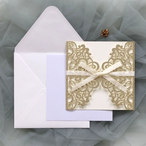 Detail of laser-cut gold glitter wedding invitation with cream silk ribbon on grey tulle