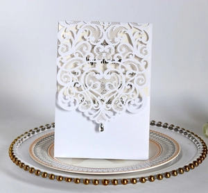 Detail of white laser-cut wedding invitation with lace patterns and a crystal pendant