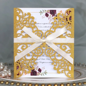Detail of laser-cut gold glitter wedding invitation with cream satin ribbon and floral insert