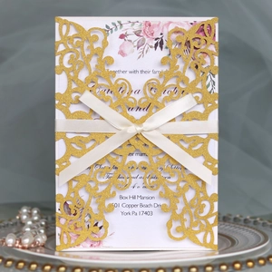 Detail of laser-cut gold glitter wedding invitation with pink floral insert and silk ribbon