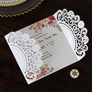 Macro detail of laser-cut lace pattern on white wedding invitation card with pink flowers