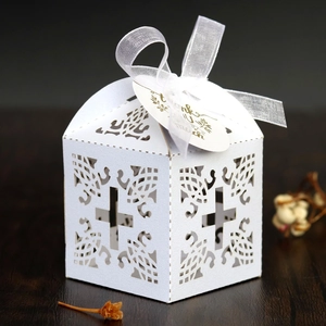 Close-up of white laser-cut wedding favor box with cross pattern and thank you tag