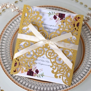 Close-up of golden glitter laser-cut wedding invitation with ivory ribbon and floral details