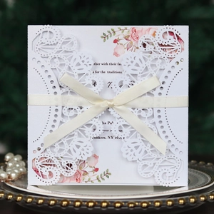 Detail of laser-cut lace wedding invitation with a cream silk ribbon bow on a gold plate