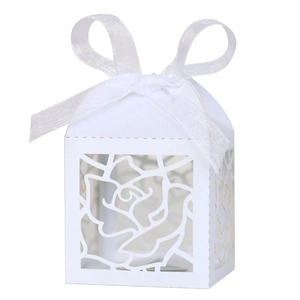 Detail of laser-cut rose patterns on a white wedding favor box with a satin ribbon bow