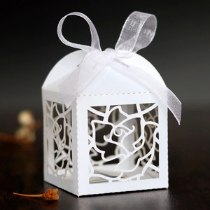 Macro detail of laser-cut rose patterns on elegant white wedding candy box with ribbon