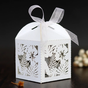 Close-up of white laser-cut gift box with tropical leaf patterns and a silk ribbon bow