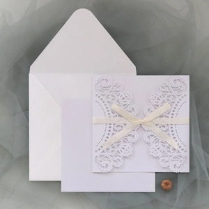 Close-up of laser cut wedding invitation with lace patterns and cream satin ribbon bow