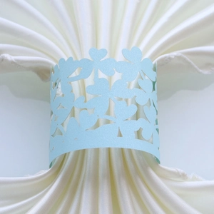 Detail of light blue laser-cut clover pattern paper napkin ring on white fabric