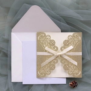 Detail of glitter laser cut wedding invitation with white ribbon bow and inner card