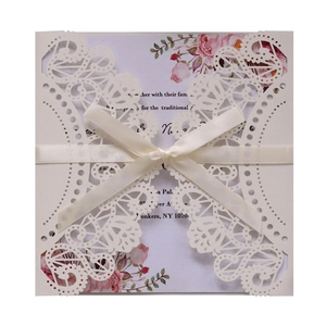 Detailed laser-cut ivory wedding invitation with floral insert and cream satin ribbon bow