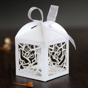 Detail of white laser-cut favor box with hollow rose pattern and white silk ribbon