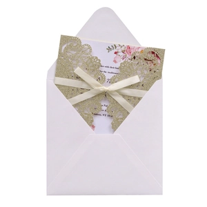 Close-up of glitter laser cut lace invitation sleeve with white satin ribbon and floral card