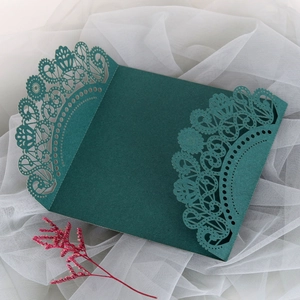 Teal laser-cut lace wedding invitation cover on white tulle background with pink flower