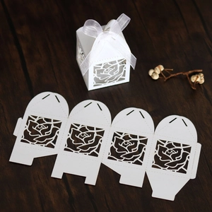 Macro view of white laser cut rose paper favor box with silk bow on wood background