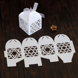 Detailed laser-cut white favor box with star patterns and satin ribbon on wood surface