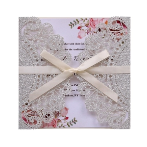 Macro shot of silver glitter laser-cut lace invitation with white satin ribbon and floral card