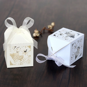 Detail of laser-cut hibiscus and leaf favor boxes with ribbons on wood table