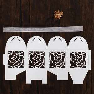 Flat lay of laser-cut white rose paper candy box template with silver ribbon on wood