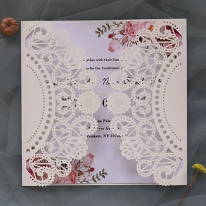 Detail of laser-cut lace wedding invitation with floral insert on a soft mesh background