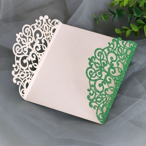 Detail of laser-cut ivory and green glitter paper wedding invitation with floral patterns