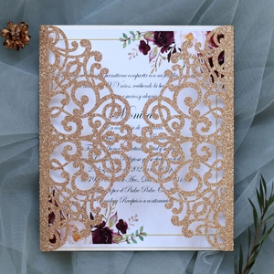 Detail of laser-cut glitter gold wedding invitation with floral insert and blue tulle background