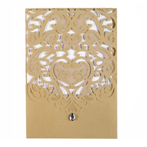 Detail of laser-cut gold wedding invitation with lace pattern and teardrop rhinestone