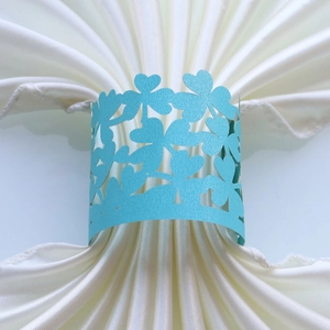 Macro detail of laser-cut light blue clover napkin ring on white satin fabric
