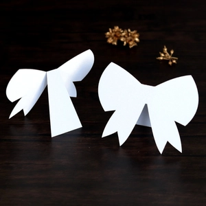 Detailed view of elegant white 3D bow place cards on a dark wood grain background