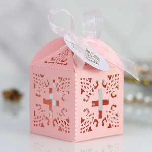 Detail of pink laser-cut wedding favor box featuring a cross pattern and white silk ribbon