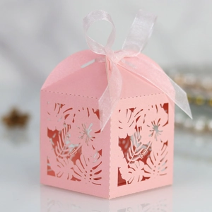 Close-up of pink laser-cut candy box featuring tropical leaf patterns and a silk ribbon bow