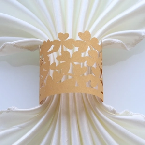 Detail of laser-cut gold pearlescent paper napkin ring with clover pattern on white fabric