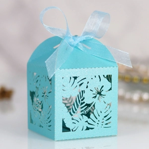 Macro detail of laser-cut light blue favor box with tropical leaf patterns and ribbon