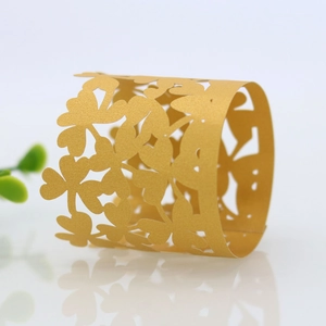 Macro view of gold laser-cut paper napkin rings with hollow four-leaf clover pattern