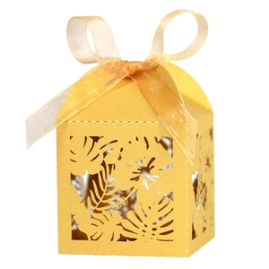 Macro detail of laser-cut tropical leaf patterns on a gold candy gift box with ribbon