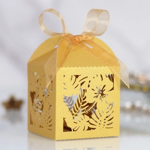 Detail of laser-cut gold wedding favor box with tropical leaf patterns and silk ribbon