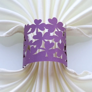 Detail of purple laser-cut paper napkin ring with clover pattern on white cloth