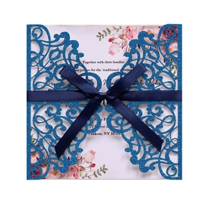 Macro detail of laser-cut glitter blue invitation with navy ribbon and floral insert
