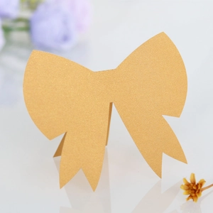 Close-up of golden 3D bow-shaped wedding place card with pearl luster finish on white surface