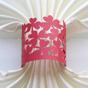 Detail of red hollow clover napkin ring with laser-cut heart on cream satin fabric