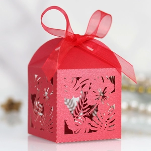 Close-up of red laser-cut candy box with tropical leaf patterns and a sheer ribbon bow