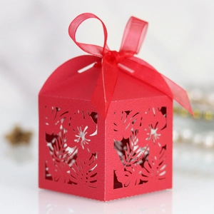 Macro shot of laser-cut red wedding favor box with intricate leaf patterns and red ribbon bow