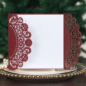 Macro detail of red laser-cut lace wedding invitation with white insert card on glass plate