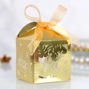 Macro view of gold laser-cut candy box with monstera leaf pattern and organza bow